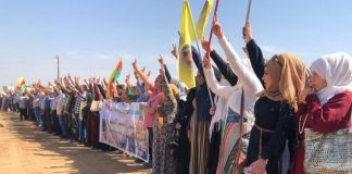 A group of people raise flags and show peace signs on a demonstration in Rojava, north-east Syria.