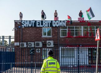 Four protesters stand on top of Elbit's building with a banner reading "Shut down Elbit" and Palestine flags.