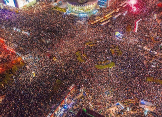 Image is an aerial view of a pro-choice rally in Poland, showing thousands of people filling a crossroads, in 2020.