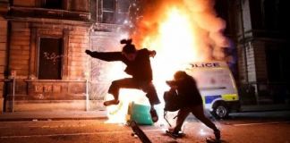An image of a cop chasing a silhouetted figure, while a police van burns in the background. Keywords; Bristol riot protesters protest peaceful violent police cops