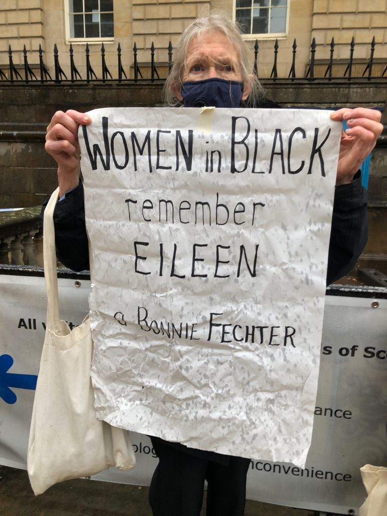 Une femme tient une pancarte indiquant 'Les femmes en noir se souviennent d'Eileen - une bonnie fechter'.