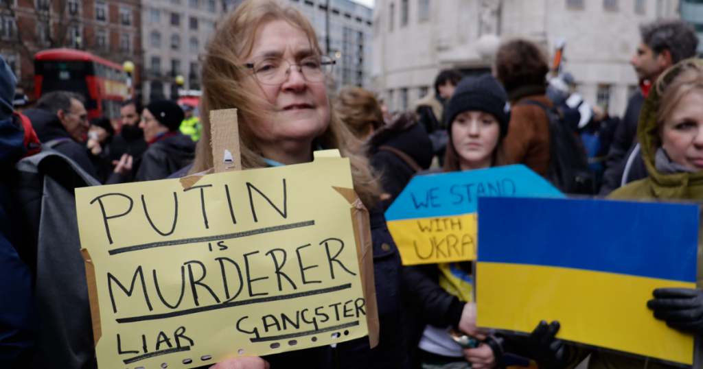Акция протеста в Лондоне 6 марта 2022 года. Плакат гласит: «Путин - убийца, лжец, гангстер».  Флаг Украины на заднем плане.  Фото Стива Изона.