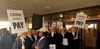 Photo taken outside Manchester Crown Court shows barristers in full robes on strike, holding placards reading 'Crime Doesn't Pay', 'Fair Pay for Fair Trials' and 'Legal Aid: Don't Lower the Bar'.