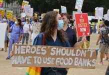 Health worker carries placard reading "Heroes shouldn't have to use food banks"