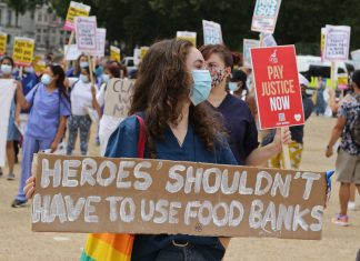 Health worker carries placard reading "Heroes shouldn't have to use food banks"