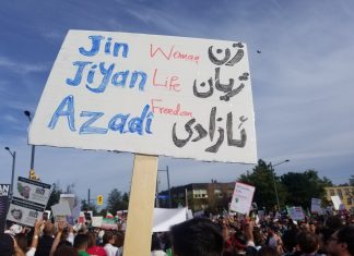 Image shows a placard against blue sky reading Jin, Jiyan, Azadi - Woman, life, freedom!