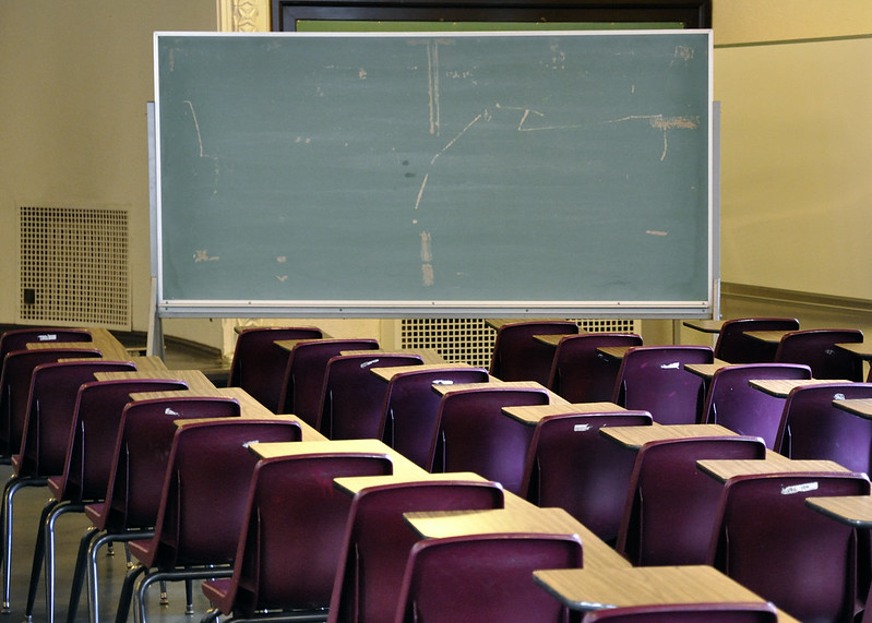 Image shows an empty classroom from the back, stacked tightly with over 30 chairs.