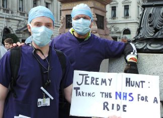 Medics in scrubs with placard reading "Jeremy Hunt: taking the NHS for a ride"