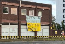 image of a single story red brick building, with a banner hanging that says 'Homes for People, Not for Profit'.