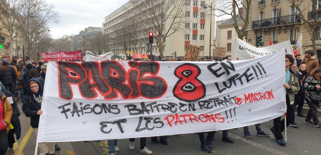 图片显示横幅上写着“Paris 8 en lutte: faisons battre en retraite Macron et les patrons”。 在英语中，这意味着“让马克龙和老板撤退”，尽管它也是退休的双关语（“la retraite”）。