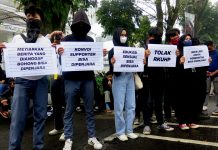 Image shows five Indonesian protesters holding signs including 'Tolak RKUHP' - "resist the criminal code". It is a mix of men and women and their faces are masked.