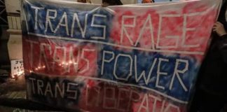 banner reading Trans Rage Trans Power Trans Liberation on pink and blue, candles in background.