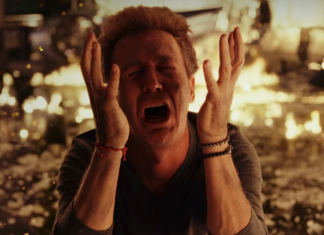 Image shows Edward Norton as his character in Glass Onion, despairing, hands up in the air and screaming, with fire in the background.