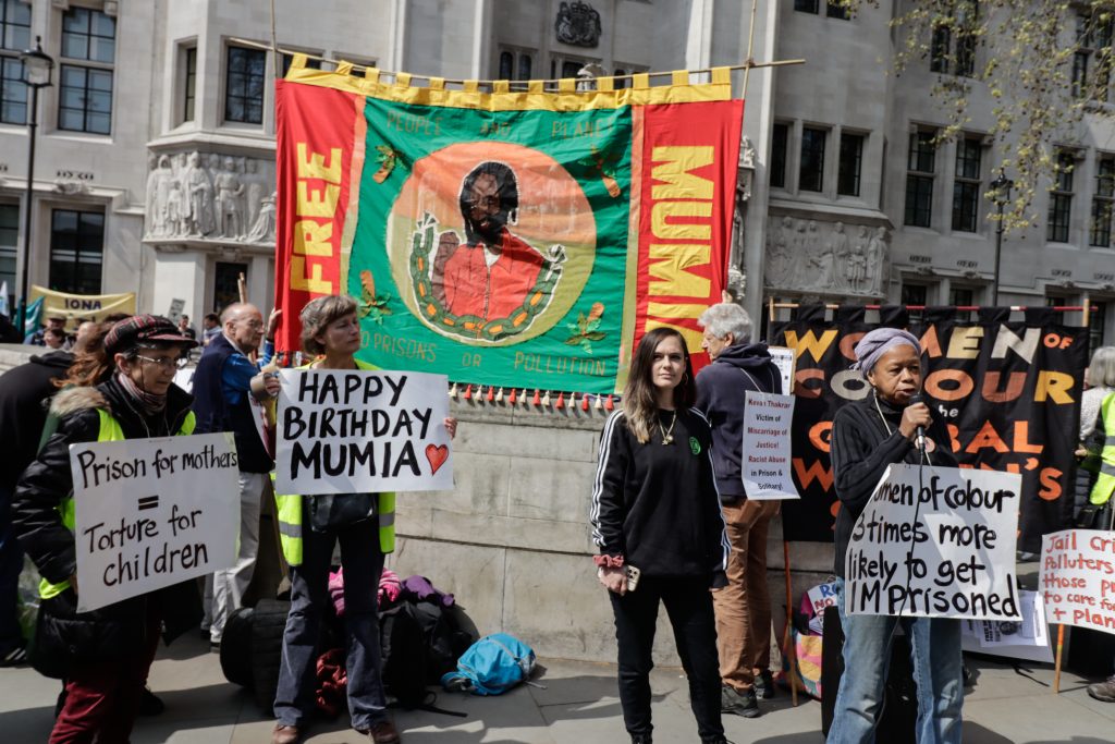 banners reading free Mumia, 'happy birthday Mumia', and a woman speaking into a microphone.