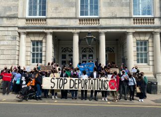 a large crowd stand outside the court with a banner reading Stop Deportations